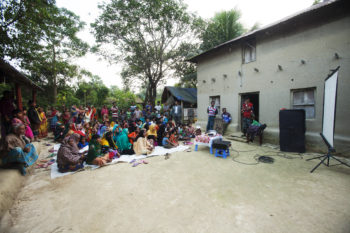 Community people watch an enter-education drama video to learn about process and services of village courts for resolving their petty disputes.